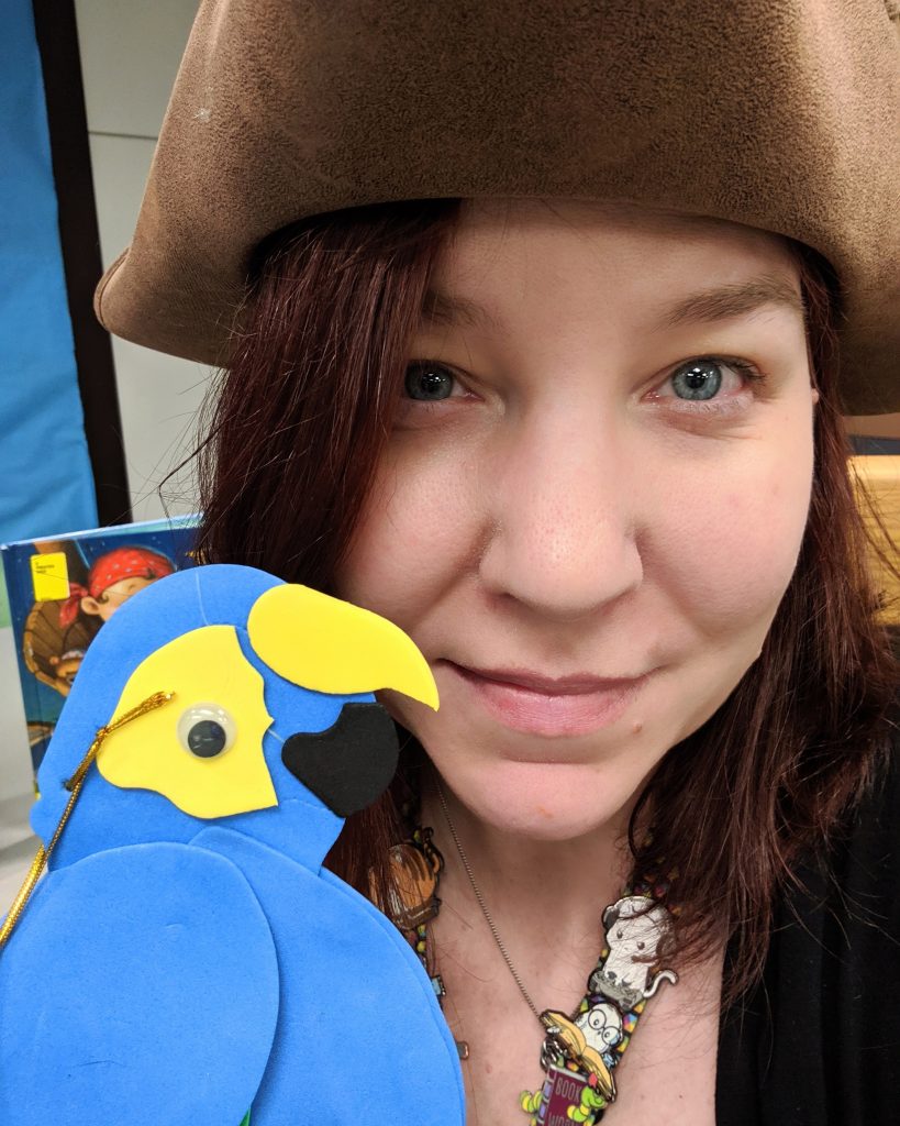 Rebecca wearing a pirate hate and holding a foam parrot - getting ready for storytime.