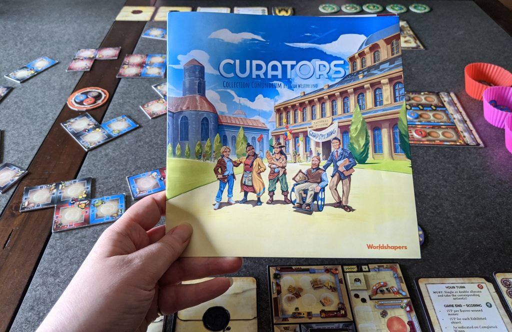 Curators rulebook held over a table with components setup on the table